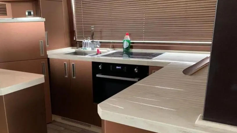 Modern kitchen featuring brown cabinetry, a sink with dish soap, and a stovetop, illuminated by natural light through blinds.